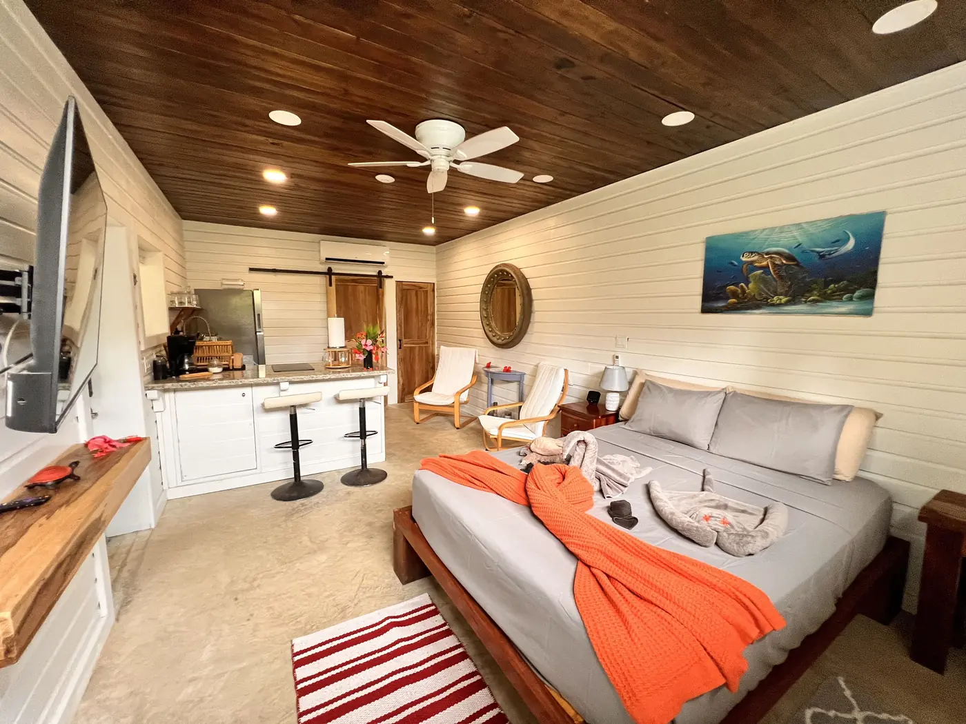 Studio interior with a queen bed, kitchen, and dark wood ceiling